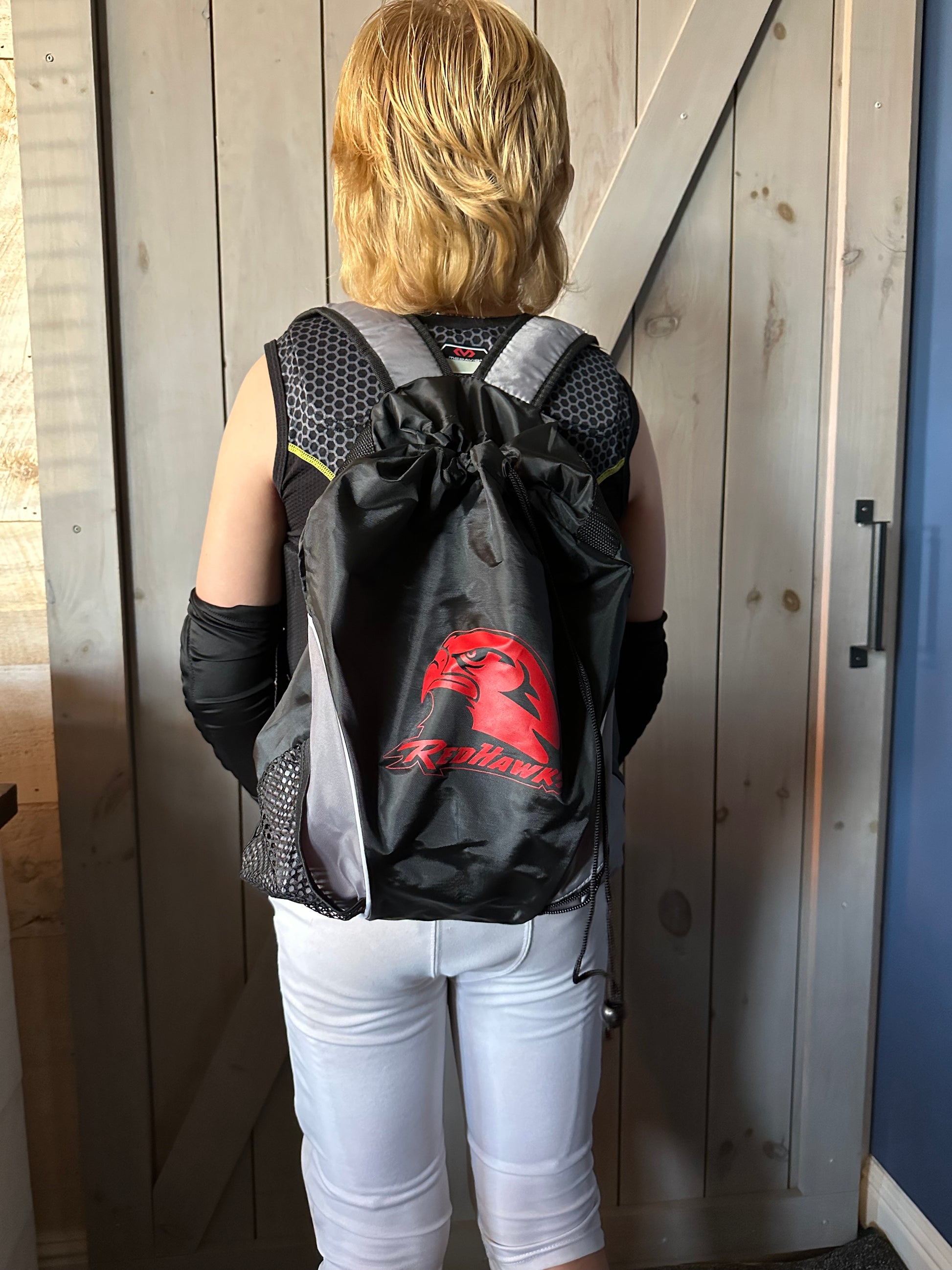 View of boy wearing backpack, black & grey w/RedHawks logo in red.