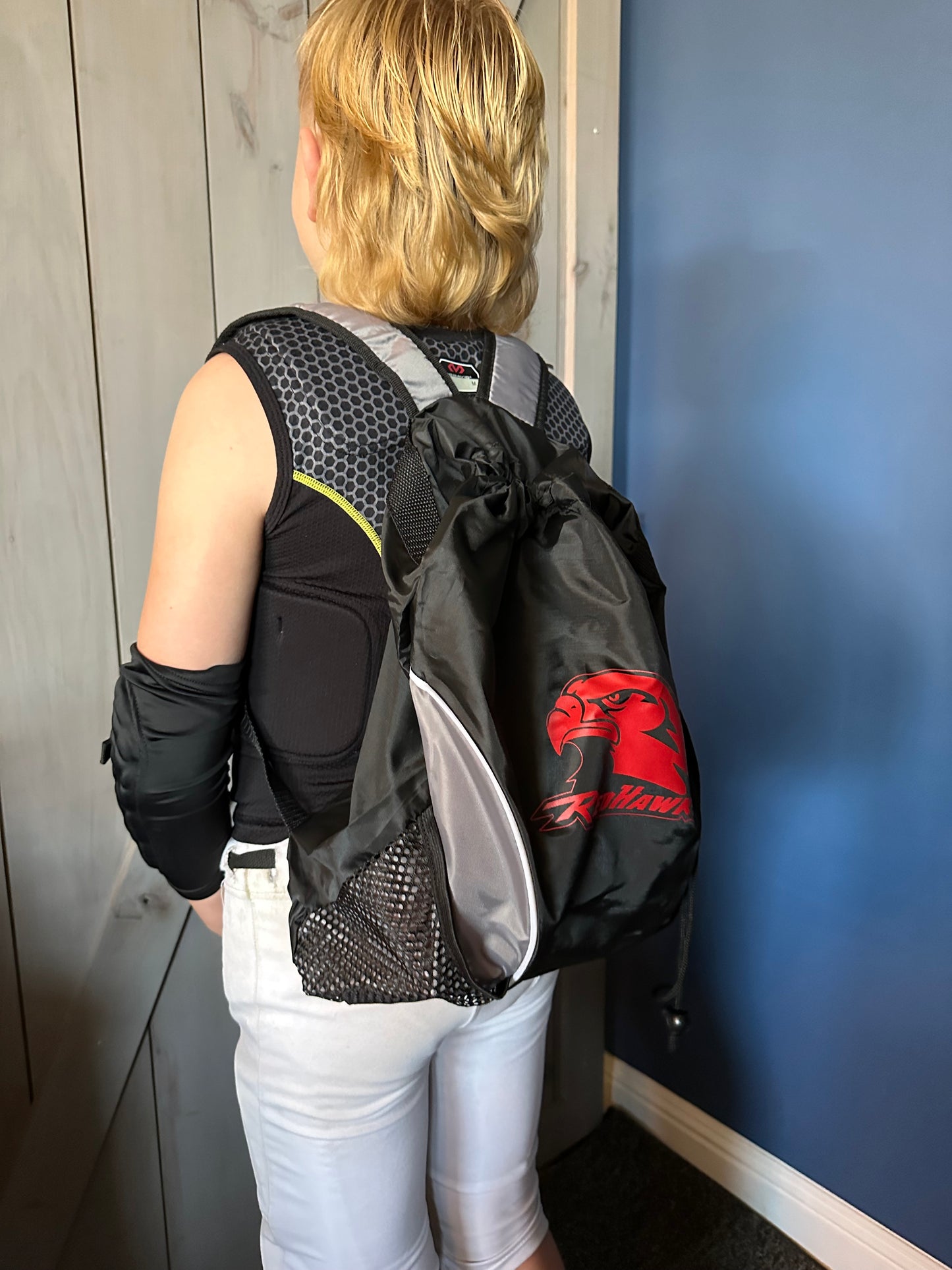 Side view, boy wearing backpack. Black and grey with RedHawks logo in red